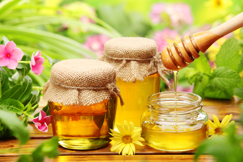 honey-in-glass-jars-with-flowers-background
