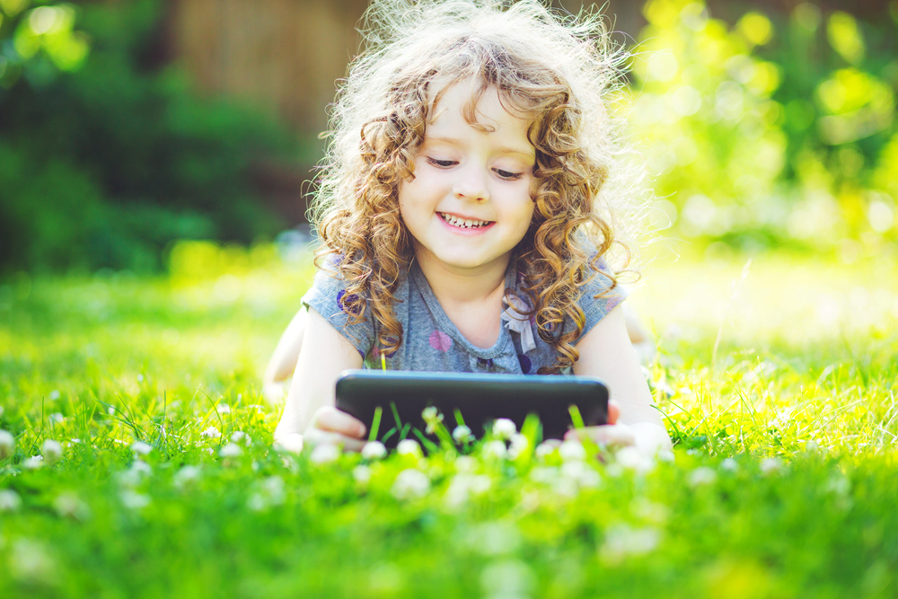 cute-curly-girl-playing-with-tablet-outdoors