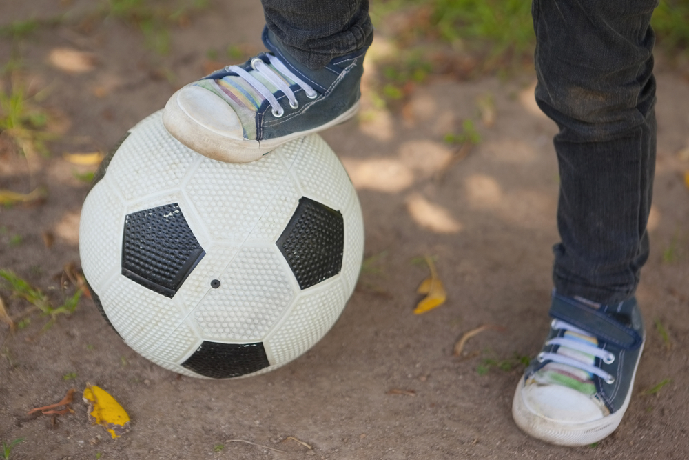 close-up-low-section-of-boy-with-one-leg-on-football-at-the-park