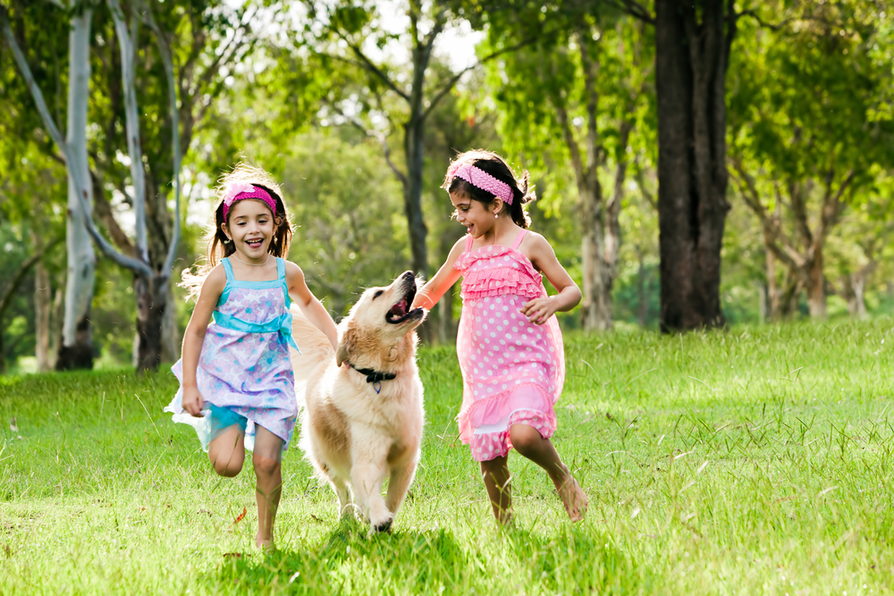 two-young-girls-running-with-golden-retriever-in-park
