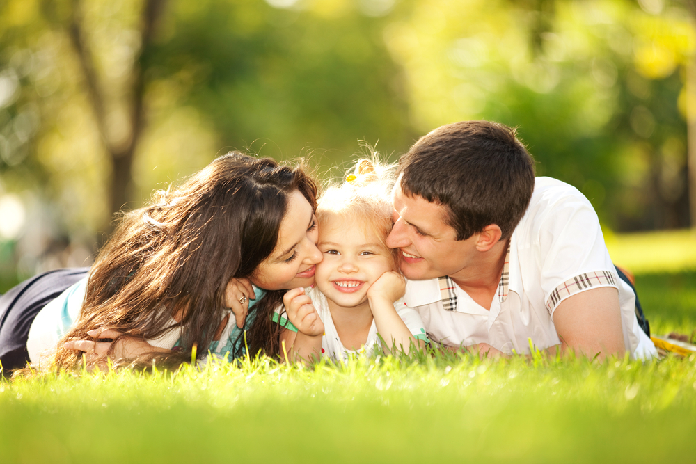 happy-mother-and-father-kissing-their-daughter-in-the-park