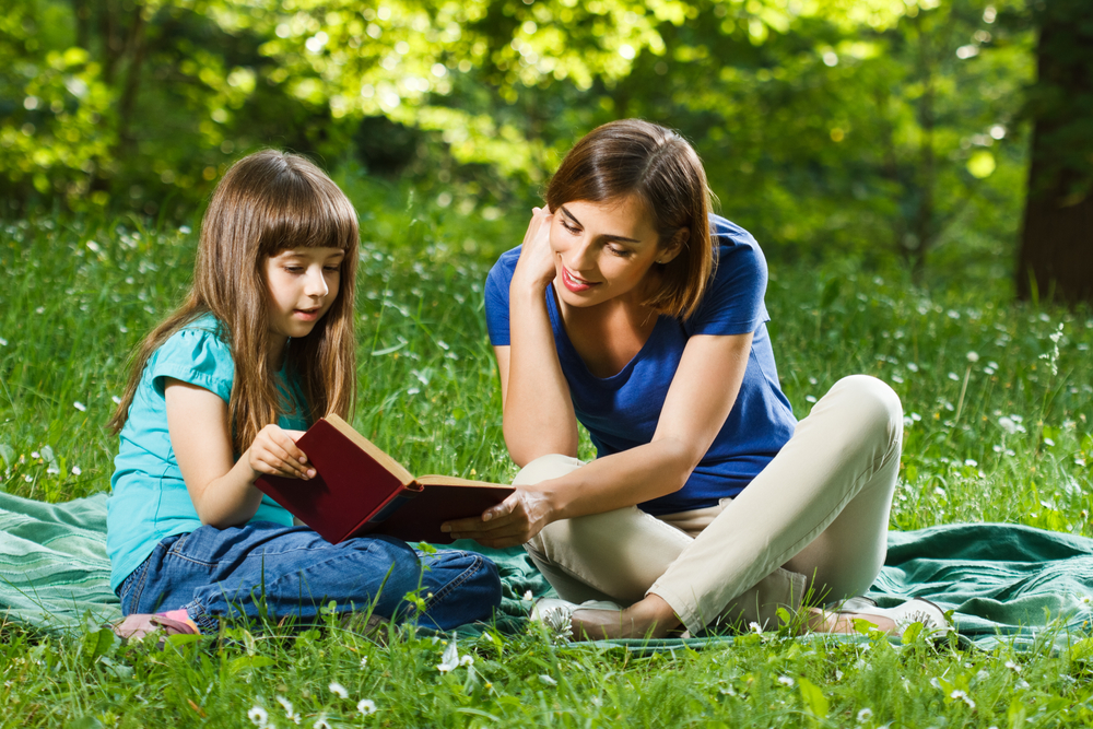 little-girl-and-her-mother-reading-a-book-while-they-sitting-and-enjoy-in-beautiful-nature