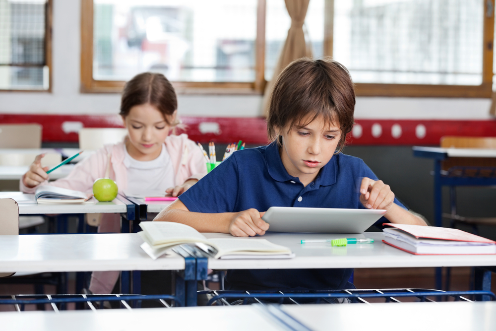 little-school-boy-using-digital-tablet-with-girl-studying-in-background-at-classroom