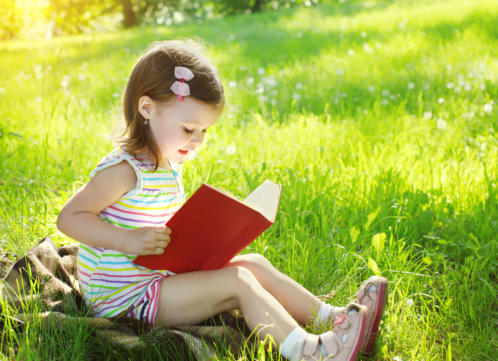 child-reading-a-book-on-the-grass-in-sunny-summer-day