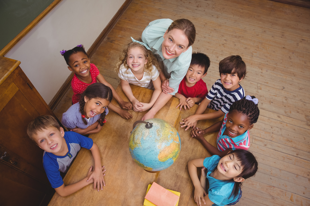 cute-pupils-smiling-around-a-globe-in-classroom-with-teacher-at-the-elementary-school